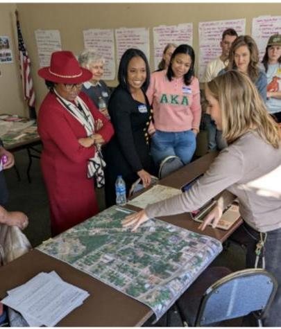 Residents and partners lean over a printed aerial site plan on a table during community planning.